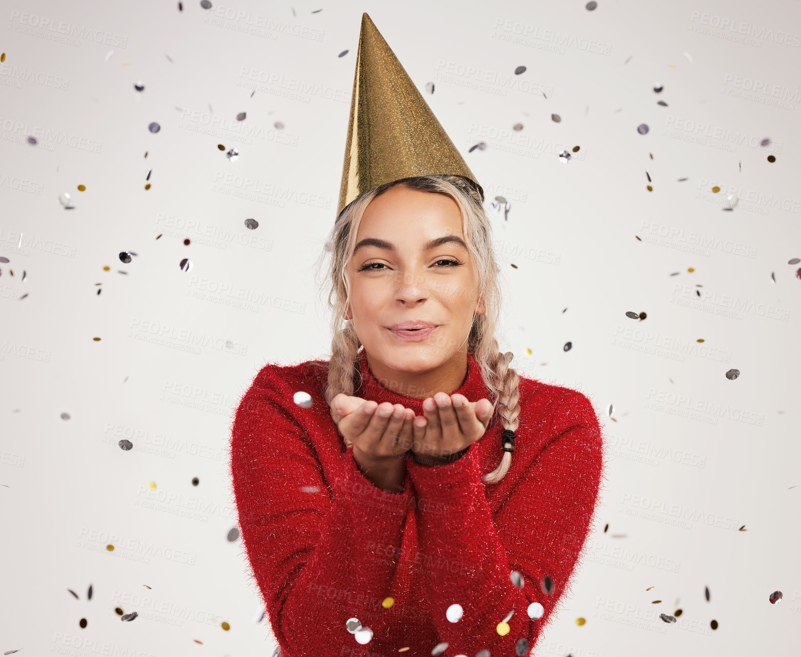 Buy stock photo Studio shot of a young woman wearing a party hat and blowing confetti against a grey background