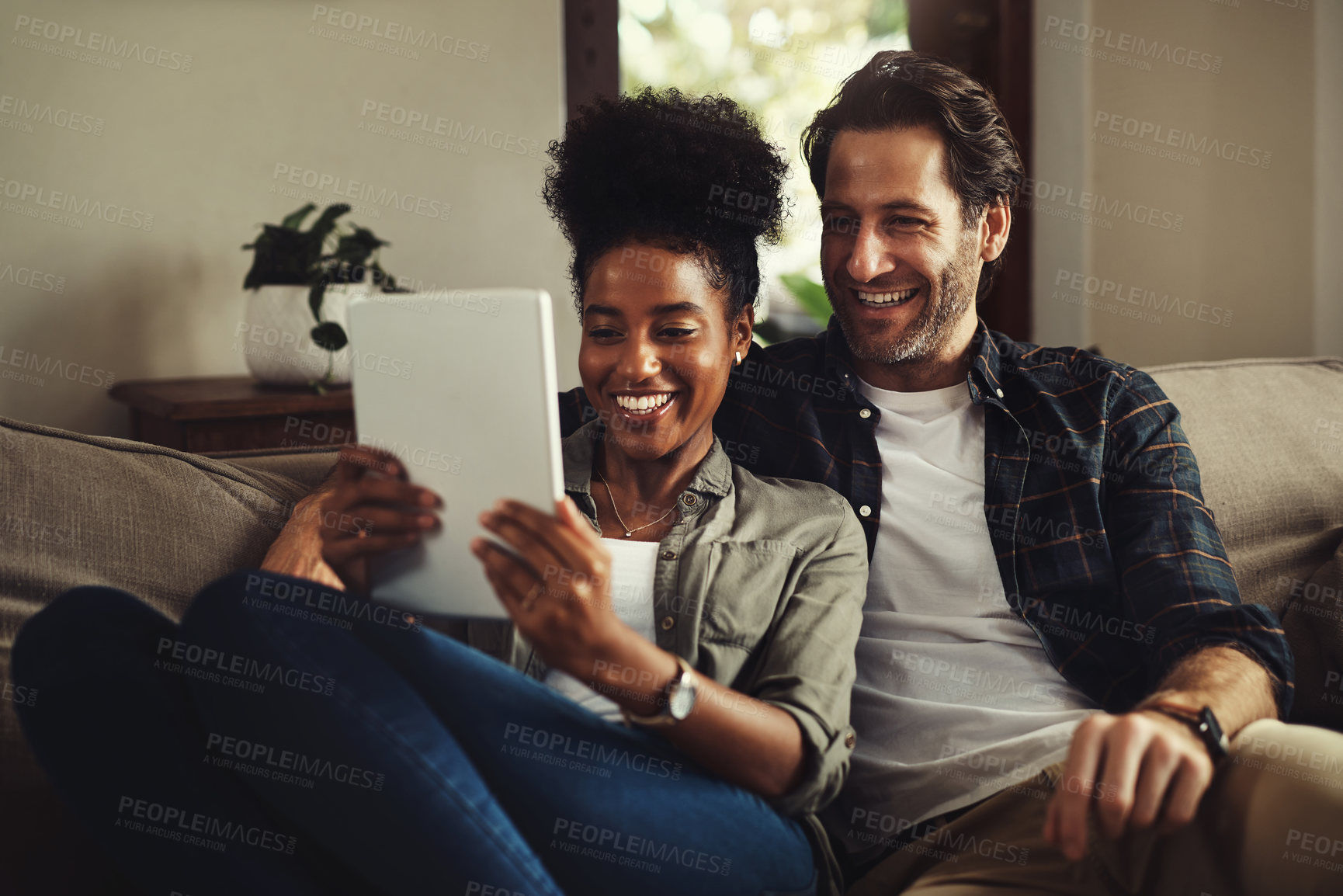 Buy stock photo Interracial couple, tablet and smile in home for media, streaming and social network on sofa. Happy man, woman or technology on couch for TV show, entertainment or ecommerce in living room on website