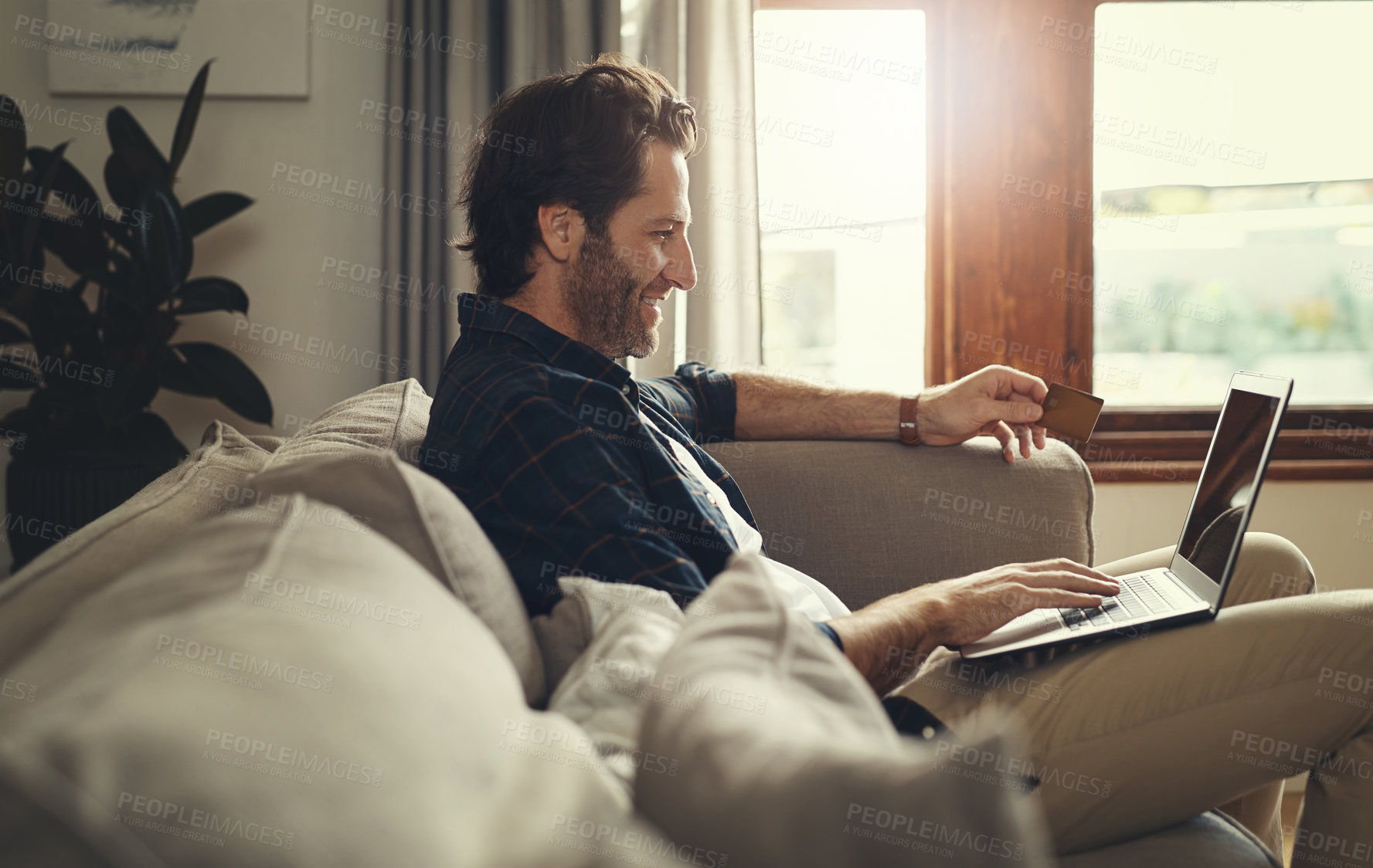 Buy stock photo Shot of a handsome young man using his laptop while relaxing on a couch at home