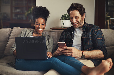 Buy stock photo Shot of a happy young couple using a laptop and cellphone while relaxing on a couch ho