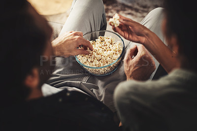 Buy stock photo Rearview shot of a young couple sitting on sofa snacking on popcorn together at home