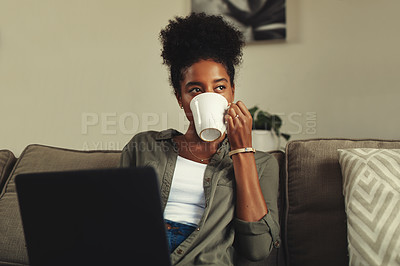 Buy stock photo Shot of a young woman enjoying a relaxing cup of coffee while using a laptop on the sofa at home