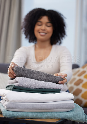 Buy stock photo Shot of a young woman sitting alone on her sofa at home and folding her laundry