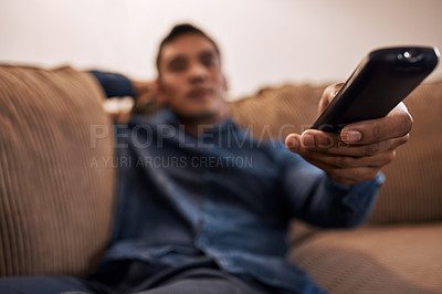 Buy stock photo Shot of a young man holding the remote while watching TV