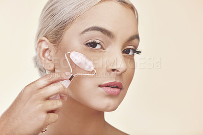 Buy stock photo Studio shot of a young woman using a jade roller on her face