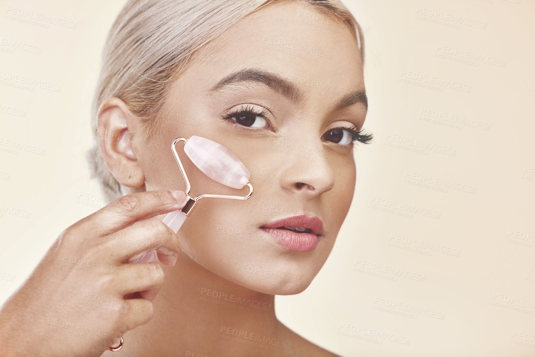 Buy stock photo Studio shot of a young woman using a jade roller on her face