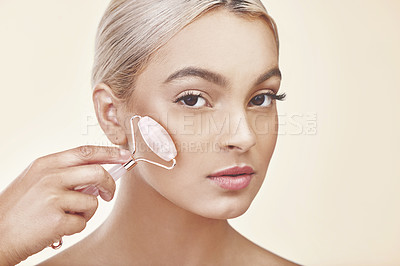 Buy stock photo Studio shot of a young woman using a jade derma roller on her face