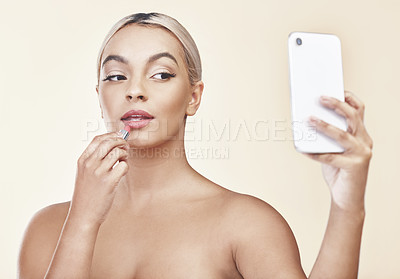 Buy stock photo Shot of a woman looking into her cellphone while applying lipstick