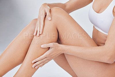 Buy stock photo Shot of a woman sitting on the floor touching her legs against a studio background