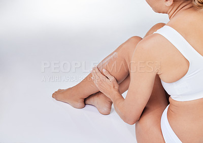 Buy stock photo Shot of a woman sitting on the floor touching her legs against a studio background