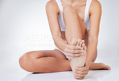 Buy stock photo Shot of a woman sitting on the floor massaging her foot against a studio background