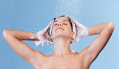 Buy stock photo Studio shot of a young woman washing her hair with shampoo while taking a shower against a blue background