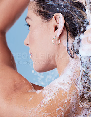 Buy stock photo Studio shot of a young woman washing her hair with shampoo while taking a shower against a blue background