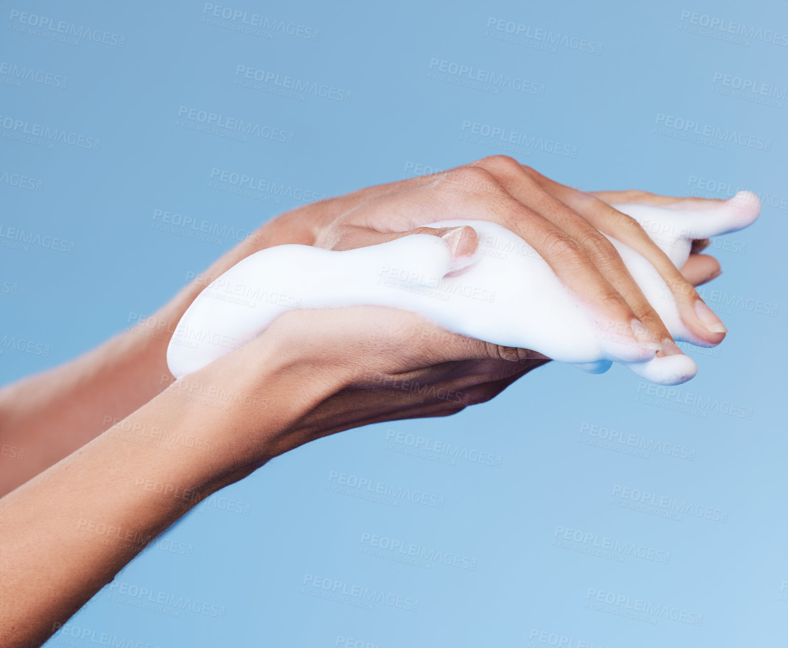 Buy stock photo Studio shot of an unrecognisable woman rubbing soap on her hands against a blue background