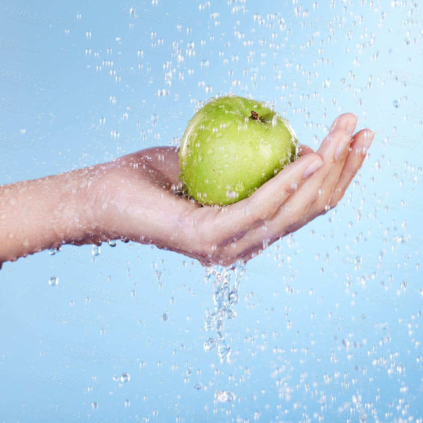 Buy stock photo Studio shot of an unrecognisable woman holding a green apple under running water against a blue background
