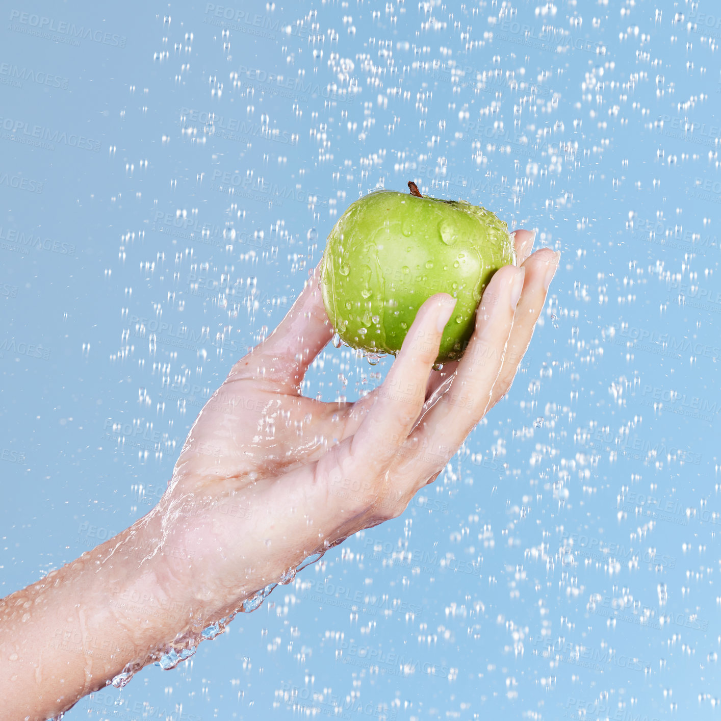 Buy stock photo Studio shot of an unrecognisable woman holding a green apple under running water against a blue background