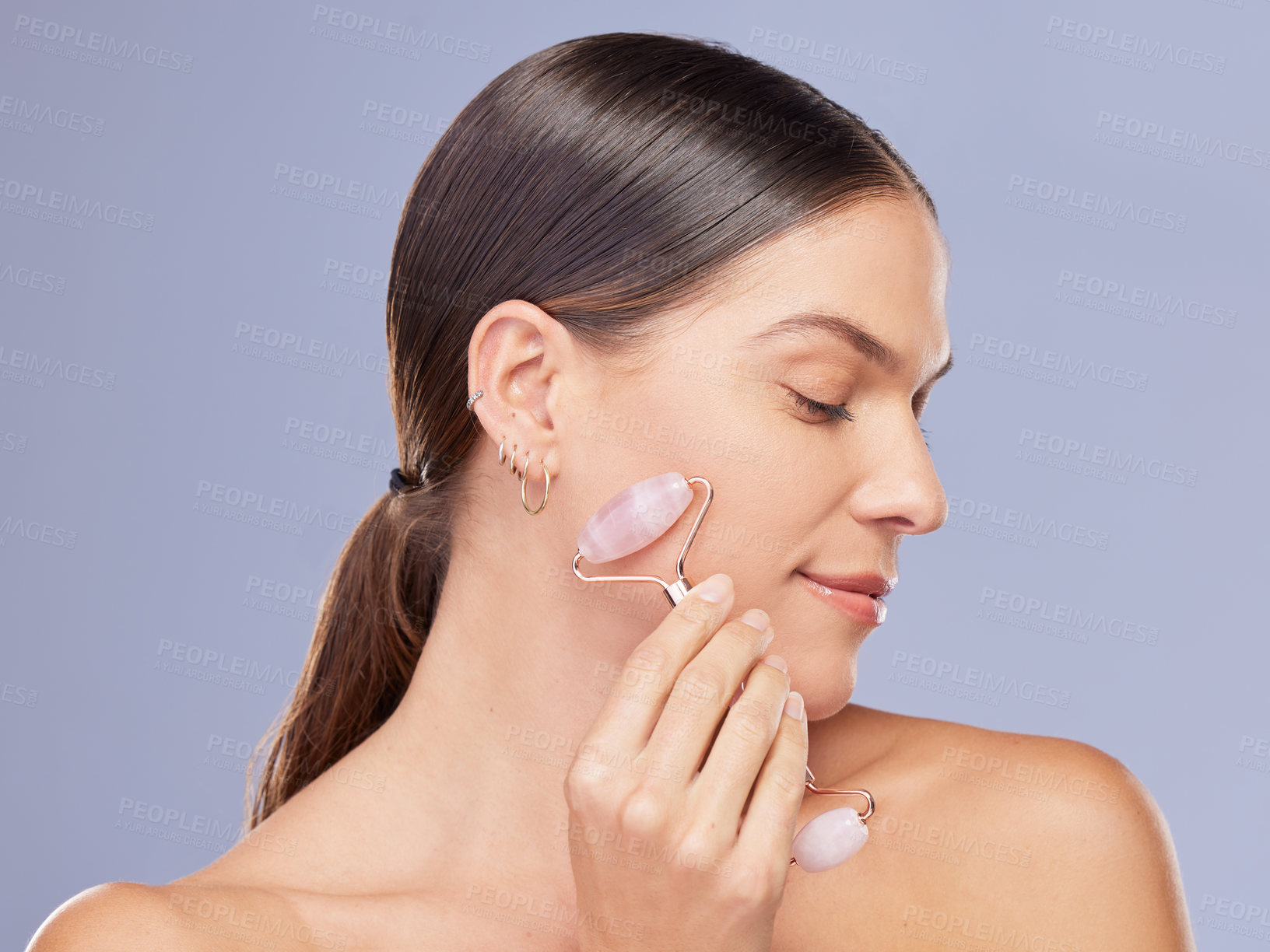 Buy stock photo Shot of an attractive young woman using a derma roller against against a purple background