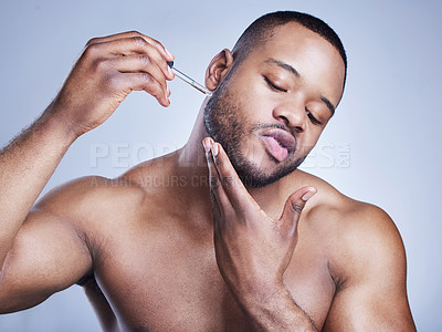 Buy stock photo Studio shot of a handsome young man applying serum to his face against a blue background