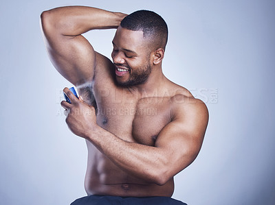 Buy stock photo Studio shot of a handsome young man applying deodorant against a blue background