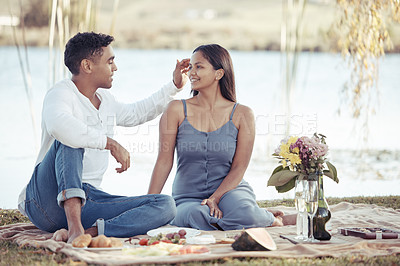 Buy stock photo Full length shot of a young couple sitting by a lake on a date and enjoying a picnic