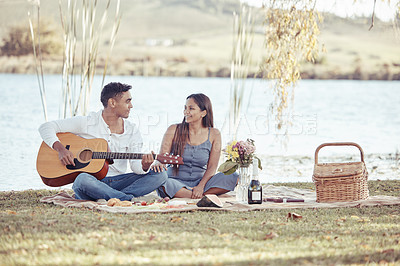 Buy stock photo Full length shot of a young woman sitting with her boyfriend while he plays the guitar during their picnic date