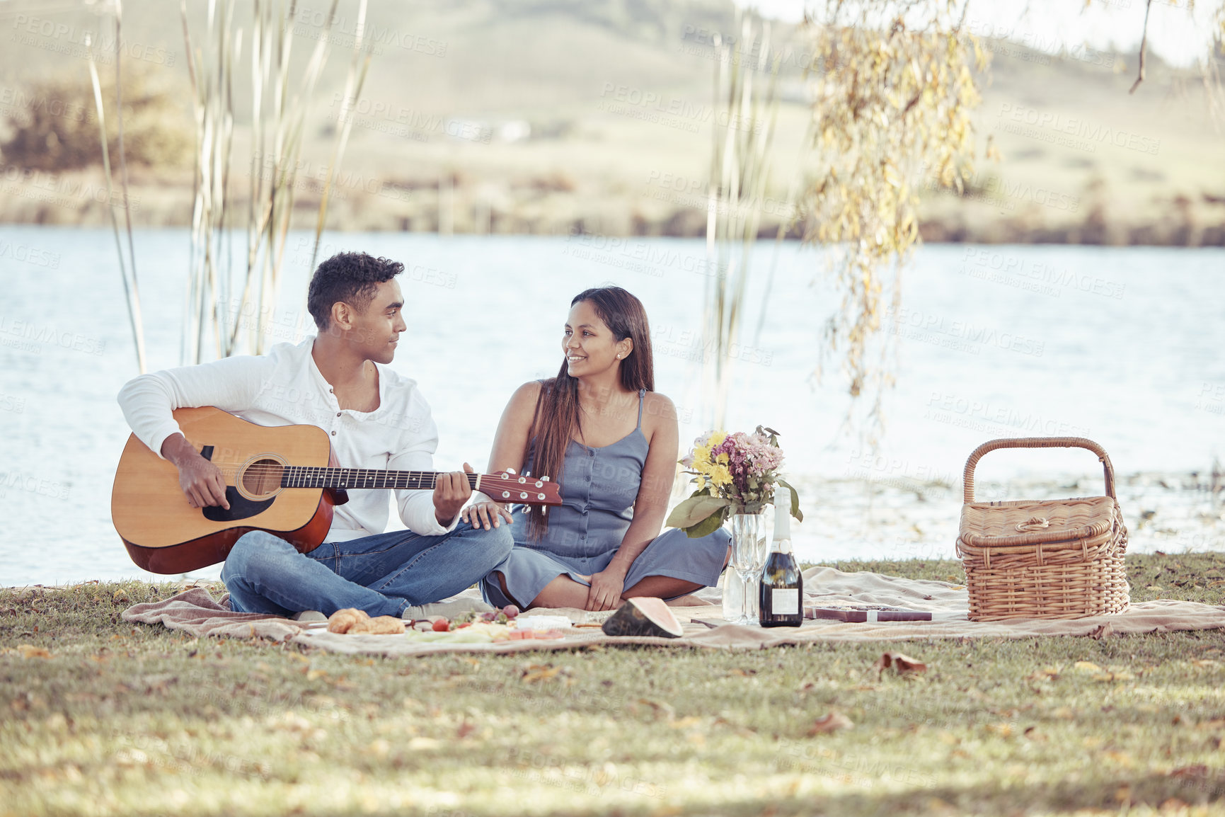 Buy stock photo Full length shot of a young woman sitting with her boyfriend while he plays the guitar during their picnic date