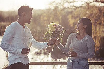 Buy stock photo Shot of a handsome young man giving his girlfriend a bouquet of flowers while on a date outdoors