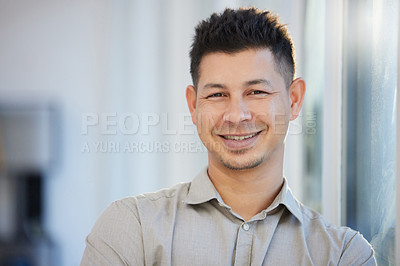 Buy stock photo Shot of a handsome young businessman standing alone in his office during the day