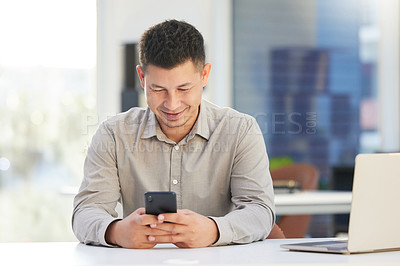 Buy stock photo Shot of a handsome young businessman sitting alone in his office and using his cellphone during the day