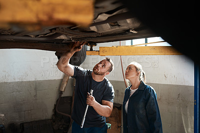 Buy stock photo Shot of two mechanics working together under a lifted car