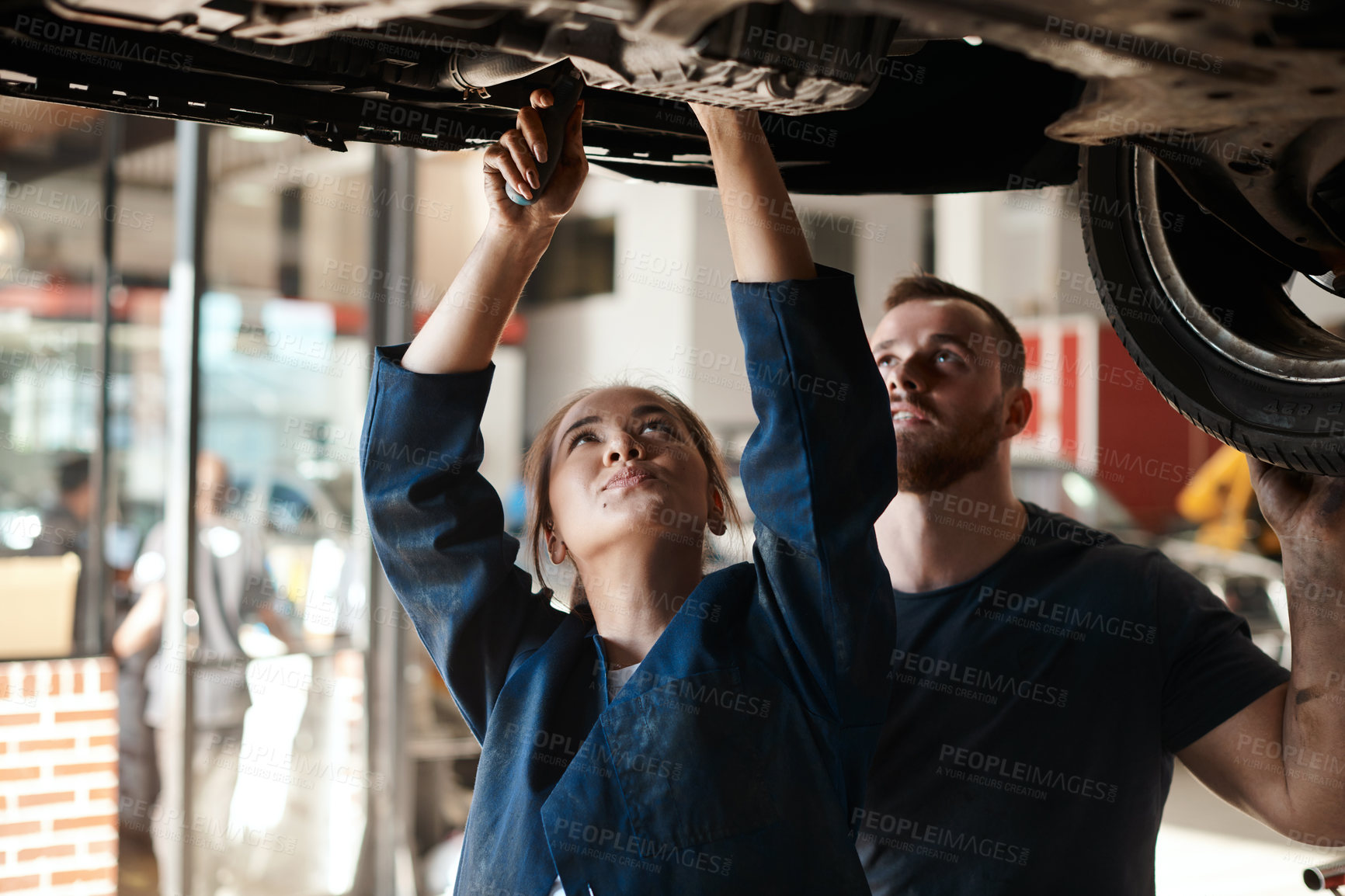 Buy stock photo Mechanic, garage and working on car with motor training, maintenance engineer and teamwork at workplace. Repair shop, tools and mentor with woman checking under with technician and auto service