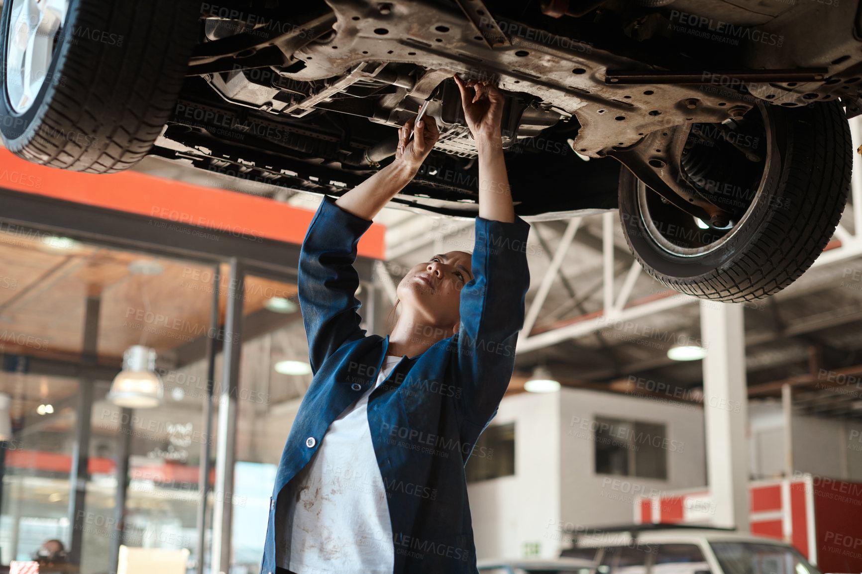 Buy stock photo Shot of a female mechanic working under a lifted car