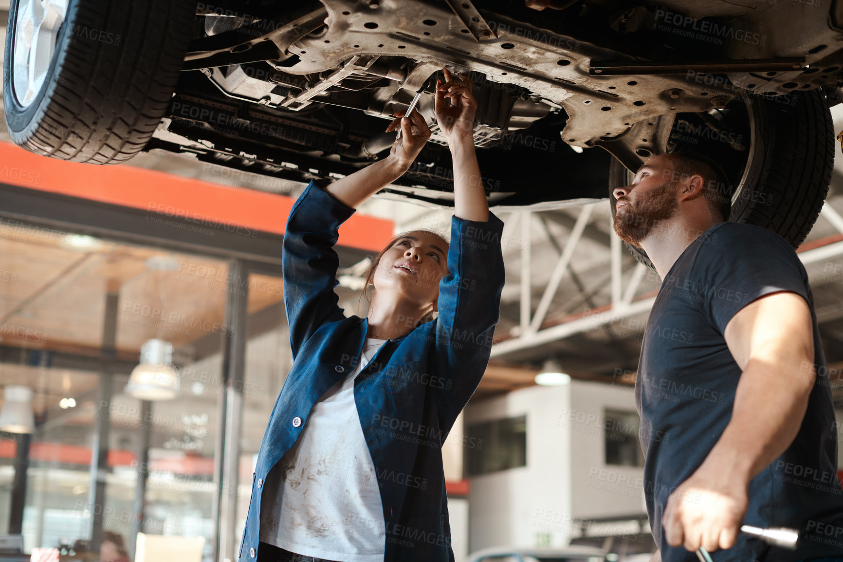 Buy stock photo Mechanic, garage work and tools for car with training, maintenance engineer and teamwork at workplace. Repair shop, trade and mentor with woman checking under wheel with technician and auto service