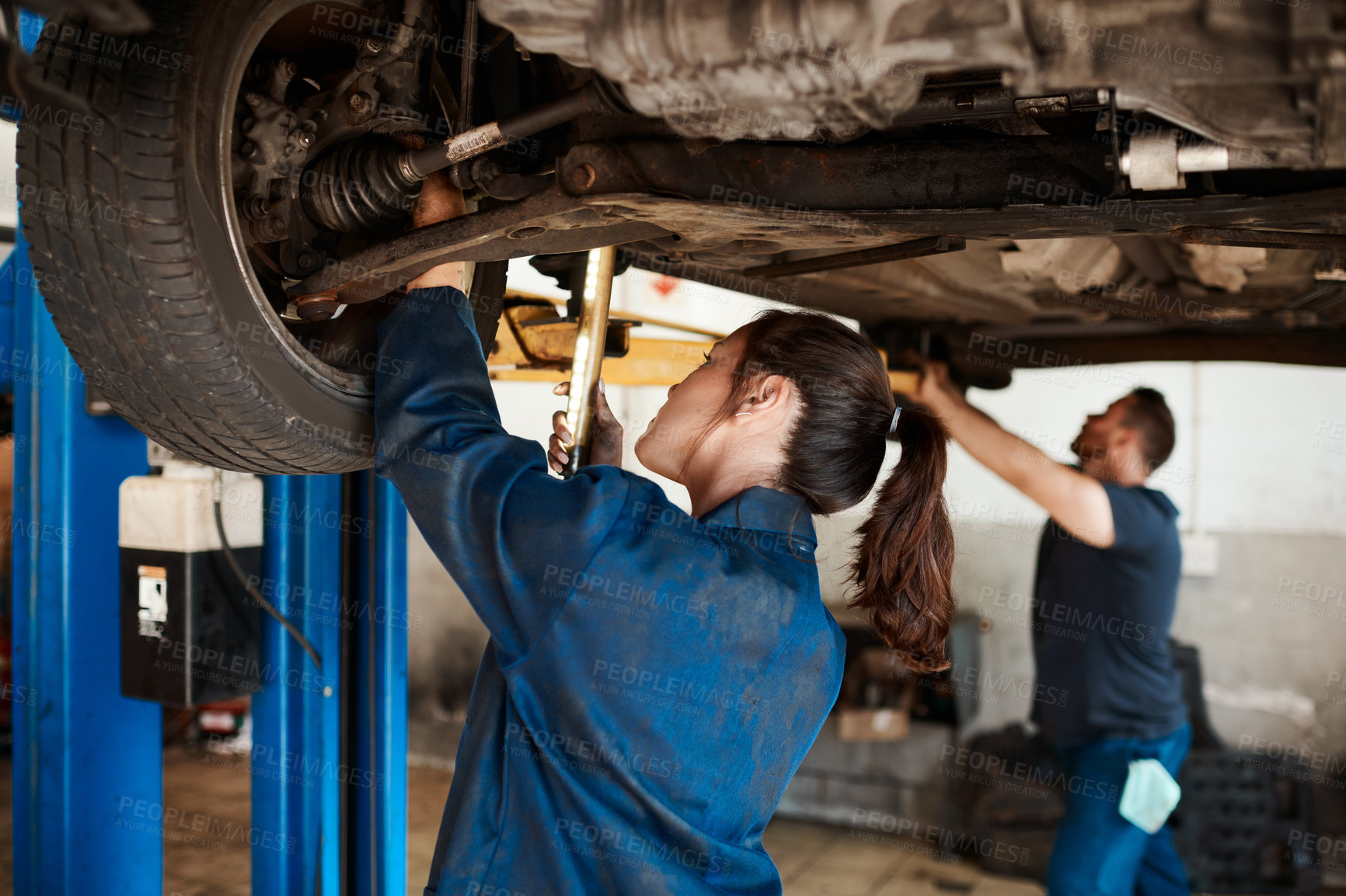 Buy stock photo Mechanic, woman and man under car in workshop for auto repair, service and inspection for safety. Engineering, partnership and teamwork for vehicle maintenance with tools, parts or industry at garage