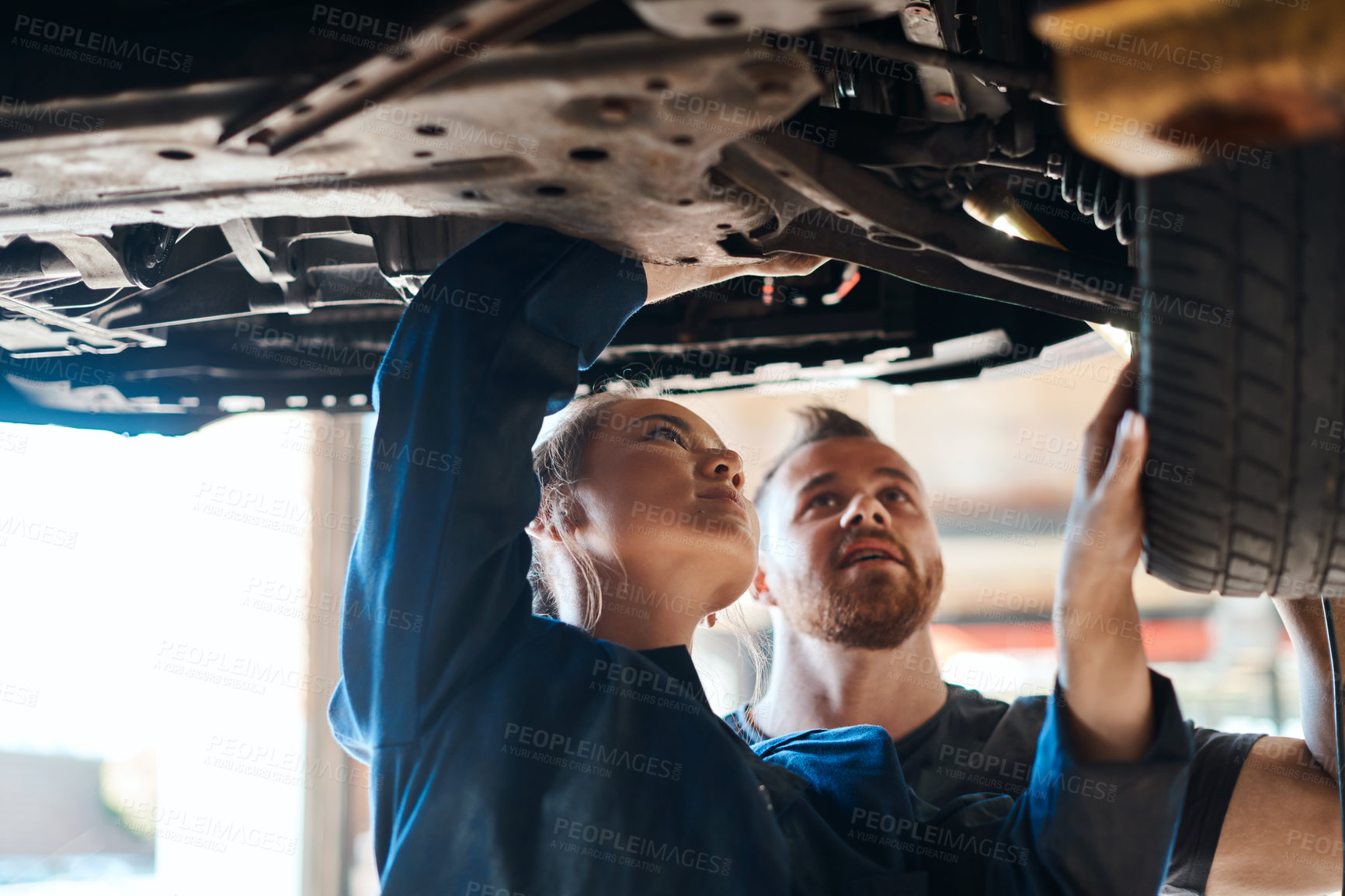 Buy stock photo Engineer, woman and man under car in workshop for auto repair, service and inspection for safety. Mechanic, partnership and teamwork for vehicle maintenance with tools, parts or industry at garage