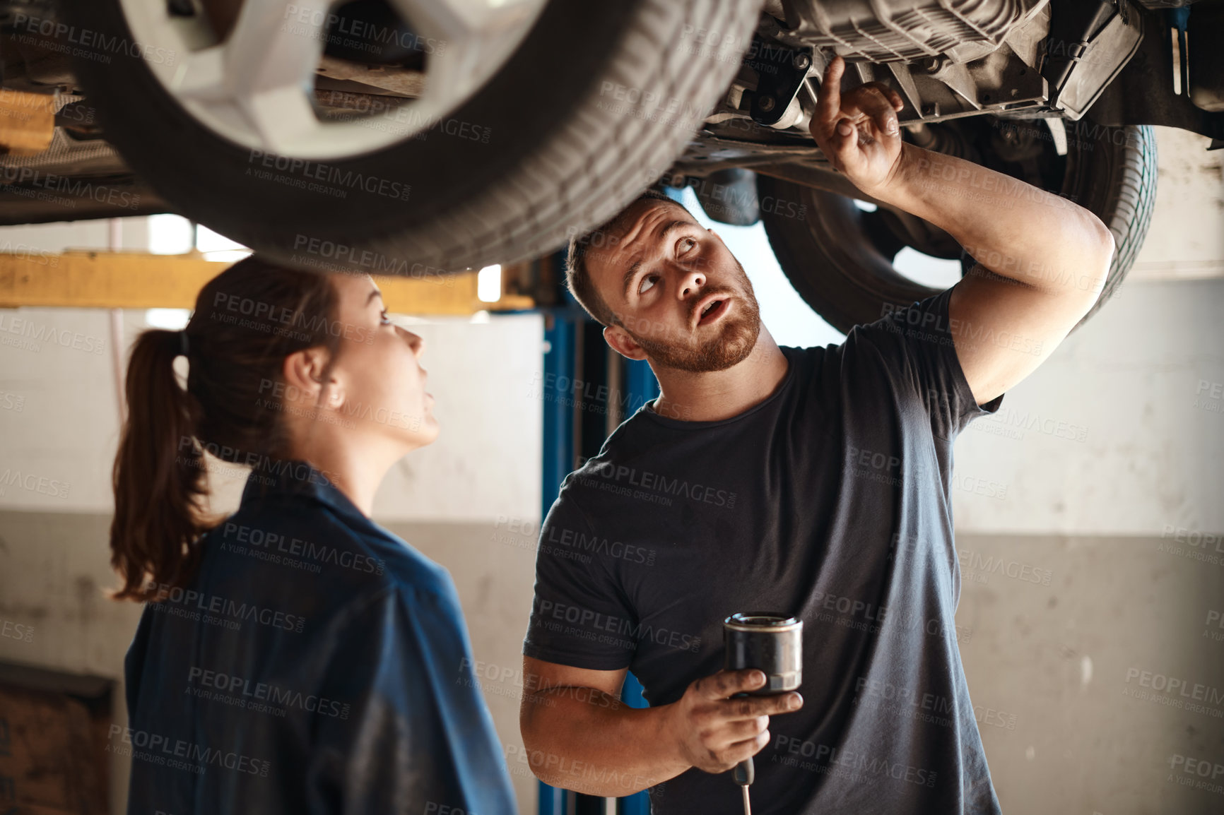 Buy stock photo Technician, woman and man under car in workshop for auto repair, service and inspection for safety. Mechanic, partnership and advice for vehicle maintenance with tools, training or industry at garage