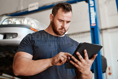 Buy stock photo Shot of a mechanic using a digital tablet while working in an auto repair shop