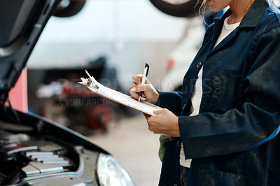 Buy stock photo Shot of a female mechanic making notes on a clipboard while working in a auto repair shop