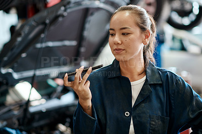Buy stock photo Shot of a female mechanic using her cellphone while working in an auto repair shop