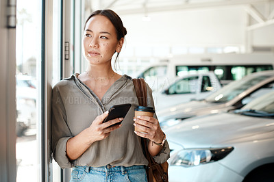 Buy stock photo Shot of a young woman using her smartphone in a car dealership