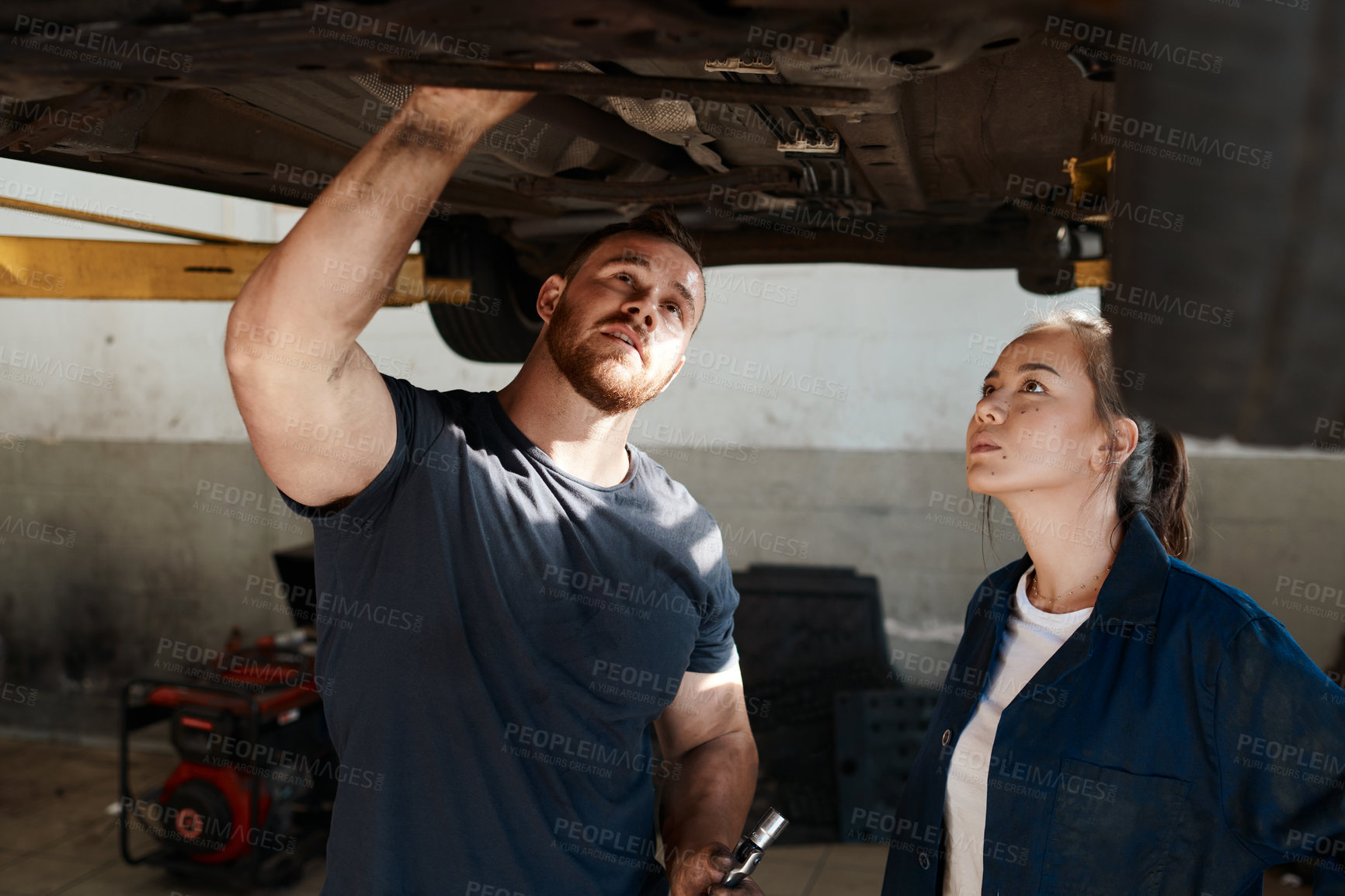 Buy stock photo Shot of two mechanics working together under a lifted car