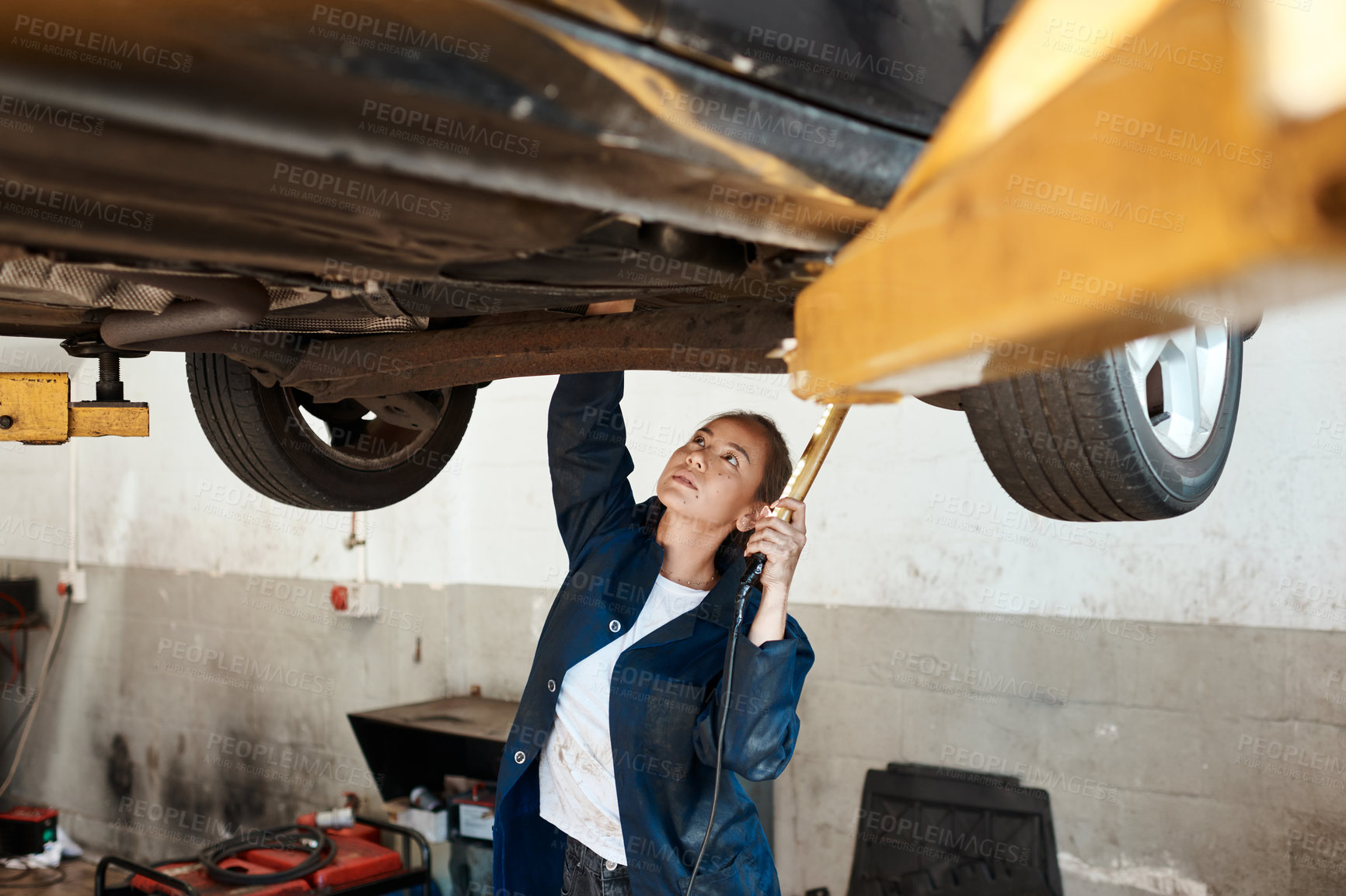 Buy stock photo Woman, inspection and car for maintenance with auto in garage, check or service on engine. Female mechanic, tool and torch for problem with motor, technician working or repair on mechanical lift