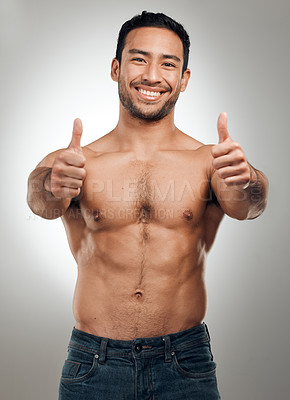 Buy stock photo Shot of a handsome young man standing shirtless in the studio and showing a thumbs up