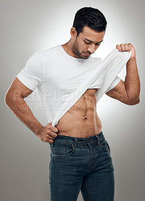 Buy stock photo Shot of a handsome young man standing alone in the studio and taking off his t-shirt seductively