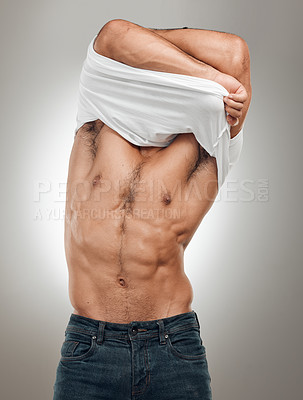 Buy stock photo Shot of an unrecognizable man standing alone in the studio and taking off his t-shirt seductively
