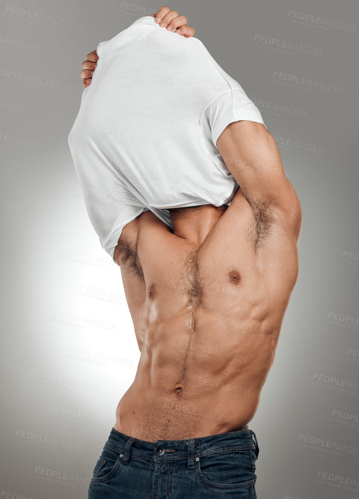 Buy stock photo Shot of an unrecognizable man standing alone in the studio and taking off his t-shirt seductively