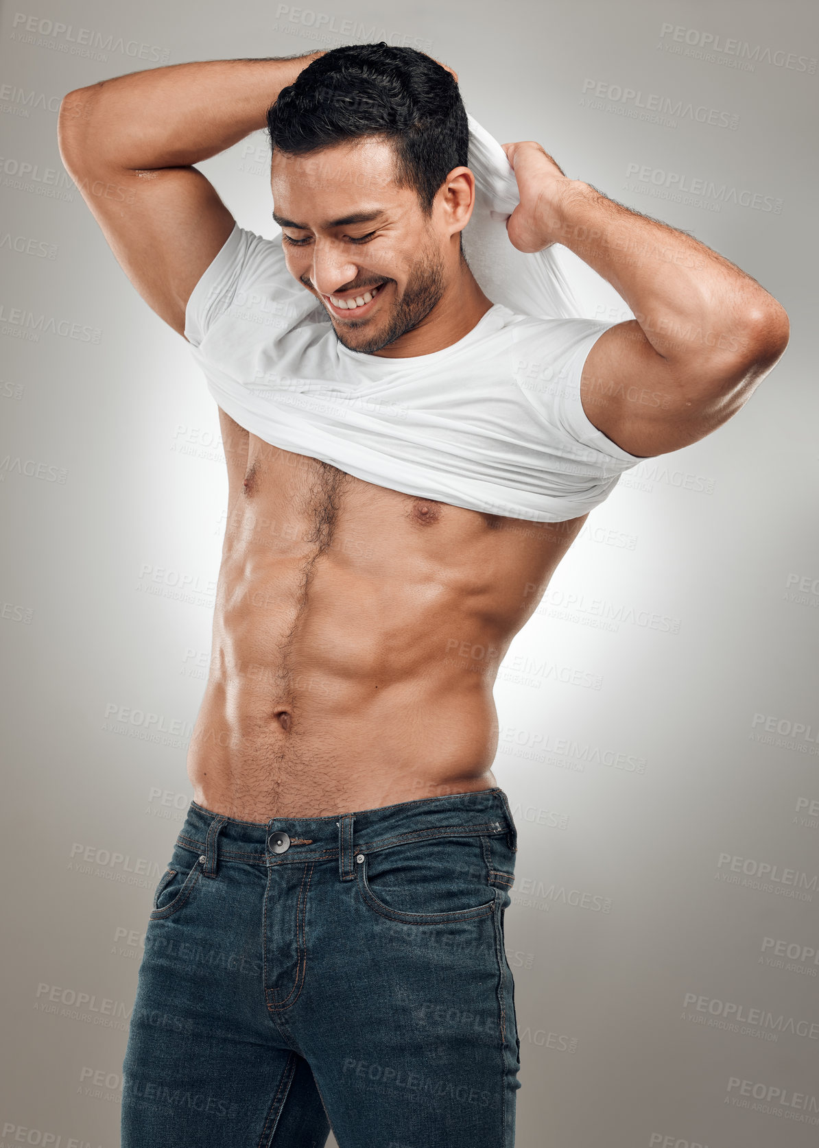 Buy stock photo Shot of a handsome young man standing alone in the studio and taking off his t-shirt seductively