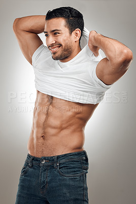 Buy stock photo Shot of a handsome young man standing alone in the studio and taking off his t-shirt seductively