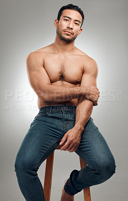 Buy stock photo Shot of a handsome young man sitting on a stool in the studio and posing shirtless