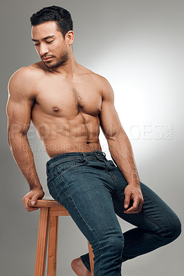 Buy stock photo Shot of a handsome young man sitting on a stool in the studio and posing shirtless